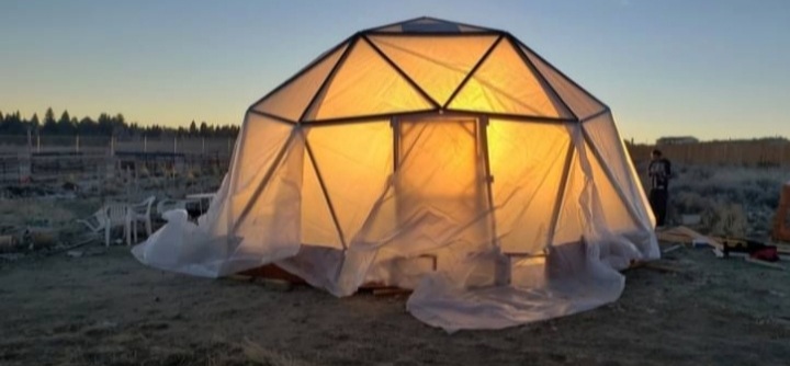 Partially finished geodesic dome greenhouse at twilight, lit from the inside