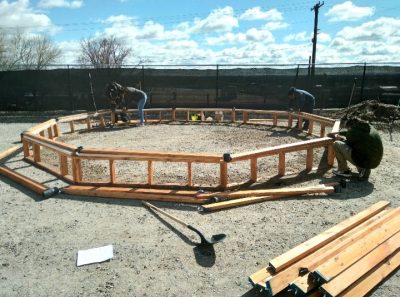 four people work on building the wooden foundation of a geodesic dome greenhouse