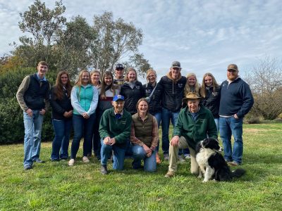 A group of fifteen people and a dog pose in a green field.