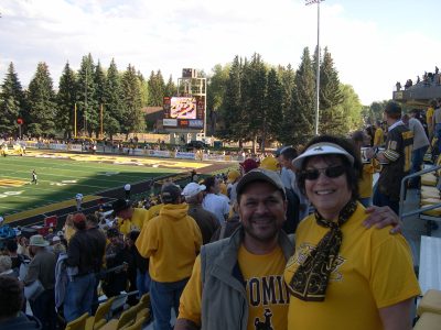 smiling man and woman wearing yellow shirts in a football stadium full of people wearing University of Wyoming brown and gold apparel