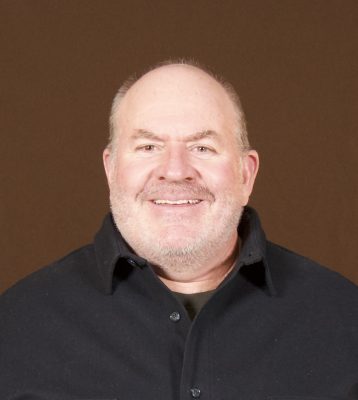 smiling balding man wearing black collared shirt
