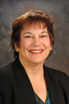 portrait of smiling woman with short brown hair wearing black blazer and turquoise earrings