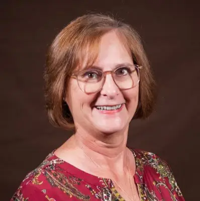 A white woman with short brown hair and glasses.