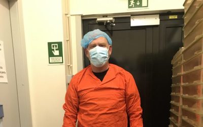 A man in bright orange scrubs wearing a hairnet, a facemask, and gloves.