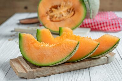 Three wedges of cantaloupe on a wooden board.
