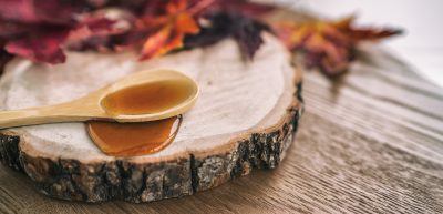 A wooden spoon with golden liquid resting on top of a thin round of wood.