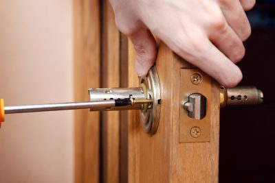 A close up on someone using a screwdriver to repair a door handle.