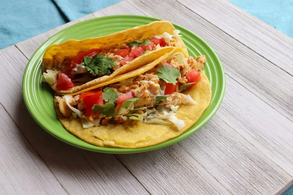 two fish tacos with vegetables on a green plate
