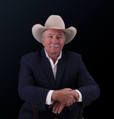 A white man in a well-fitted suit and a nice cowboy hat. He has gray hair and a short mustache. 