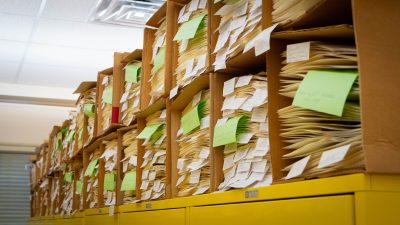 A long stack of boxes, two deep, each filled with files interspersed with occasional green post it notes.