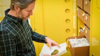 A white man with gray hair and a goatee looks down at an unfolded paper envelope, which holds what appears to be mat of dried moss.