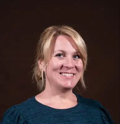 A young white woman with blonde hair in a low ponytail wearing a dark blue short sleeve shirt with somewhat puffy sleeves.
