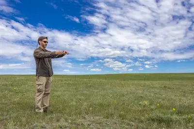 A man standing in a field with his arms straight out, holding a phone pointed at the ground.