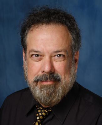 Smiling man with dark hair and beard wearing black shirt and black and gold tie