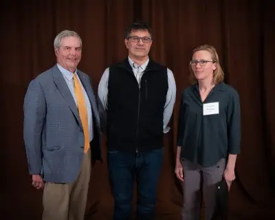 A man in a suit with short gray hair, a man with short black and gray hair with glasses wearing a vest, and a woman with bobbed blonde hair and glasses wearing a dark turquoise shirt.