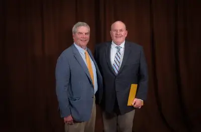 A man with short gray hair in a suit standing next to another man in a suit with cropped gray hair.