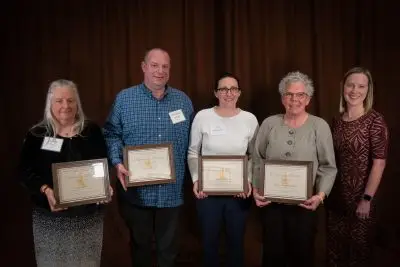 Five people wearing formal attire, four of which are holding plaques.