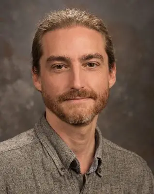 portrait of man with brown hair and short beard wearing gray collared shirt