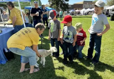 A woman holds a lamb, which is stretching out towards several children.
