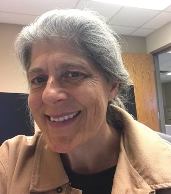 selfie photo of smiling woman with gray hair wearing tan canvas jacket