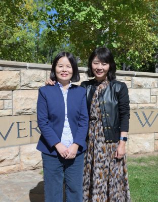 Two Chinese women standing next to each other. They both have bobbed black straight hair and light skin. The woman on the left is wearing a blue suit and the woman on the right is wearing a dress and black jacket. 