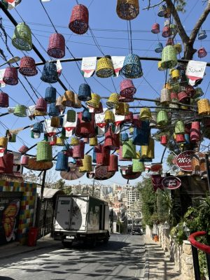 Quite a few colorful upside down baskets hang over a paved street with a city in the background.