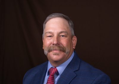 A man with short gray hair and a large mustache wearing a blue suit and red tie.