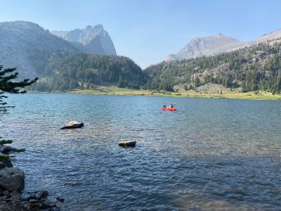 Two people in a red kayak in a mountain lake.