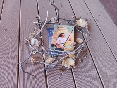 A circle of sticks, leaves, and dried flowers around two books stacked on each other, one of which is titled "Pippa's First Summer" and the other "The Talking Earth".