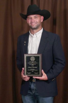 A man in a black cowboy hat and suit jacket holding a plaque acknowledging his 2024 Distinguished Service Award.