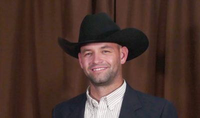 A man in a black cowboy hat and suit jacket holding a plaque acknowledging his 2024 Distinguished Service Award.