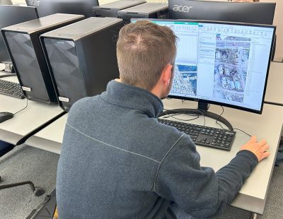 A young man looking at a computer screen. An overhead view of houses is visible on the screen. 