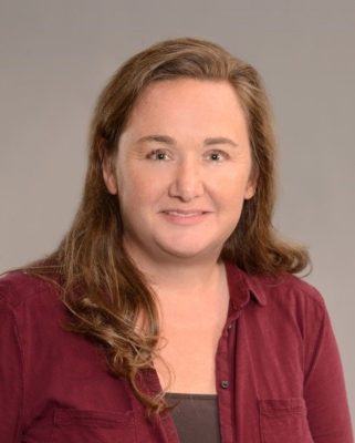 A woman with long brown hair wearing a red cardigan.