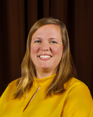 A woman with shoulder length blonde hair wearing a yellow shirt.