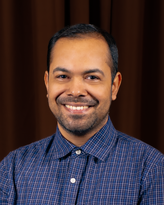 A man with short straight black hair and a short beard wearing a collared shirt. 