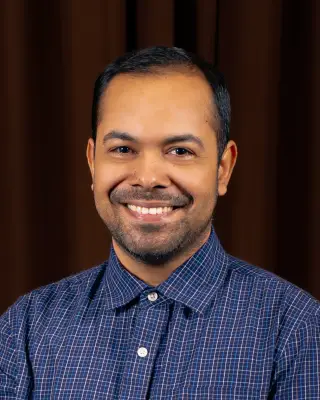 A man with short straight black hair and a short beard wearing a collared shirt.
