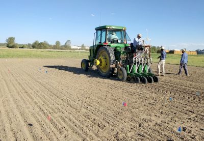 Two men seated on a tractor while two young men walk alongside in an empty field.