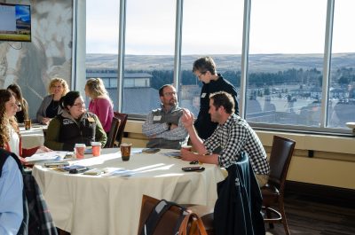 Several young adults sit at a table talking to each other. 