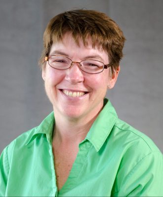 A woman with short brown hair and glasses wearing a light green shirt. 