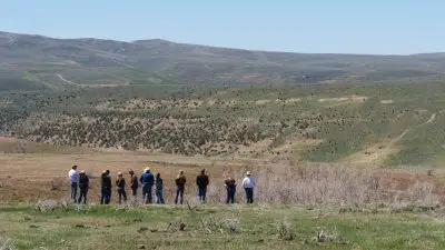 About ten people standing in a grassy, hilly landscape.