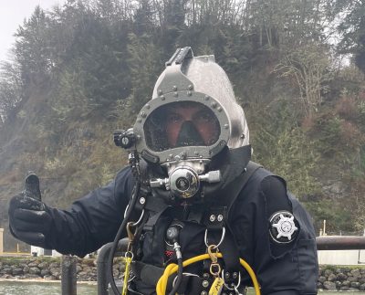 portrait of a man wearing dive gear giving a thumbs-up sign on a wet, gray day