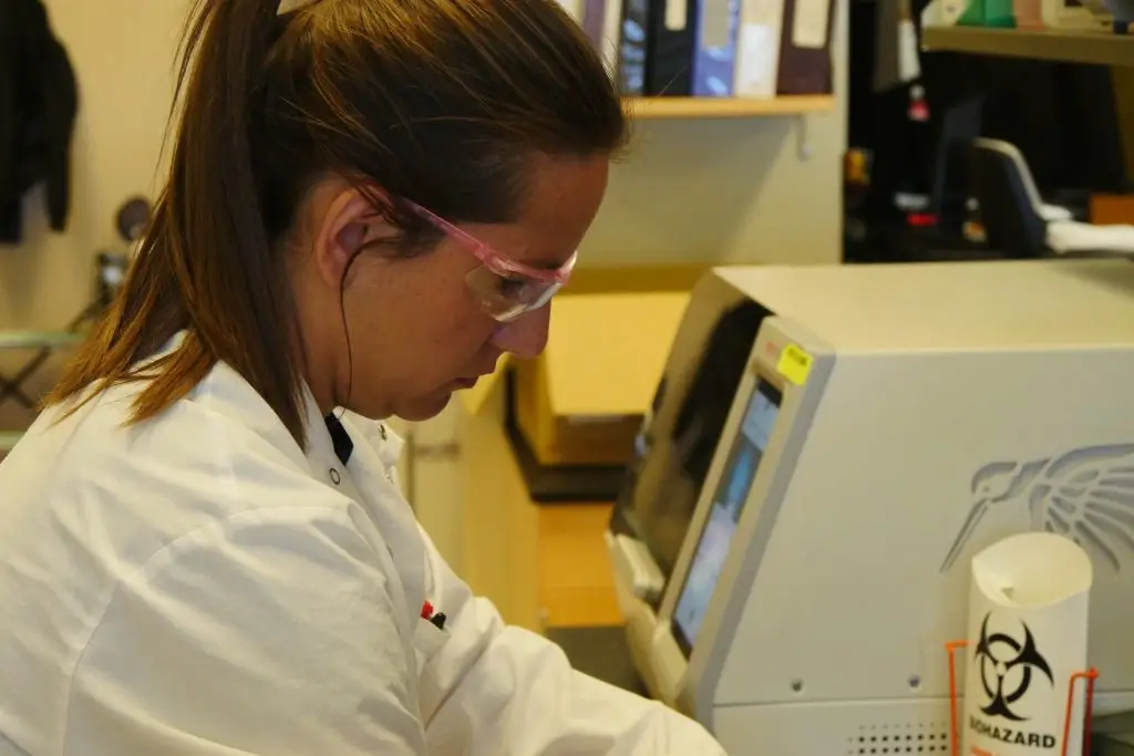 side profile of a lab technician wearing lab coat and safety glasses