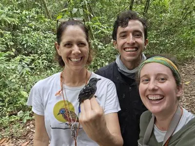 Three people smiling. One holds small black bird.