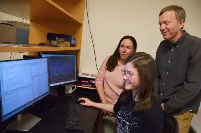 Three people look at a computer screen.
