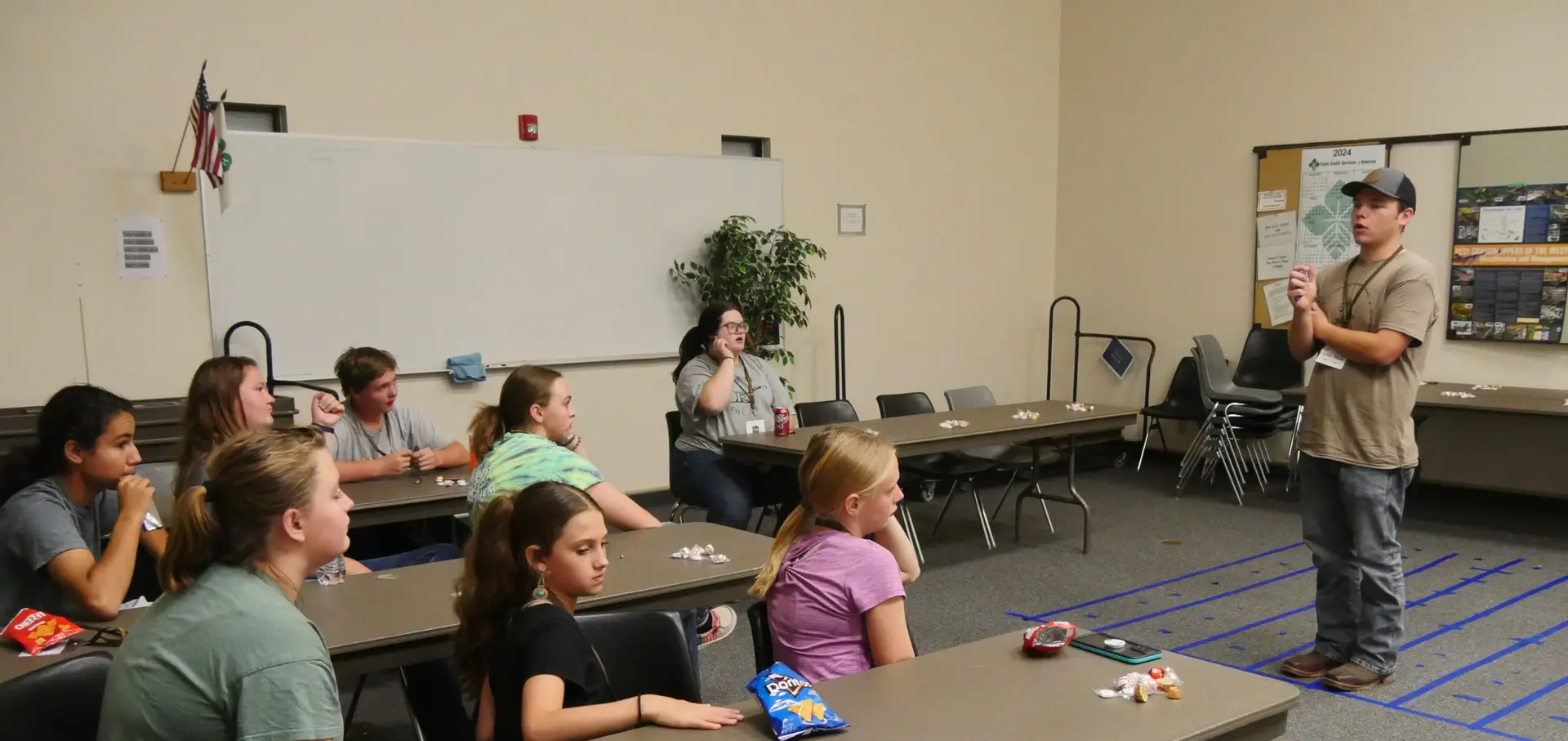 man stands in front of eight 4-H members who are seated at long tables facing toward the presenter