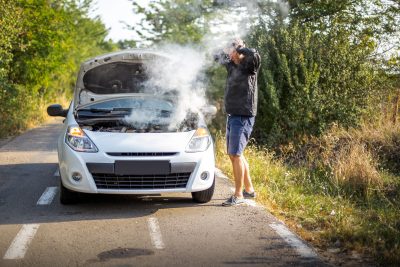 A man with his hands thrown up next to a broken down car
