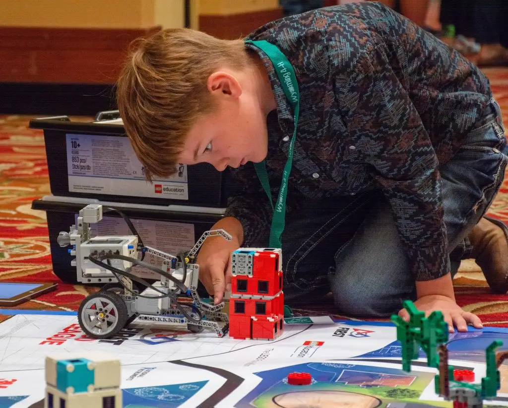 young boy kneels on the floor beside Lego vehicle on a mat