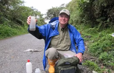 A man holding up a bottle in a rainforest setting