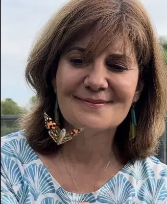 A woman smiling at a butterfly flying in front of her.