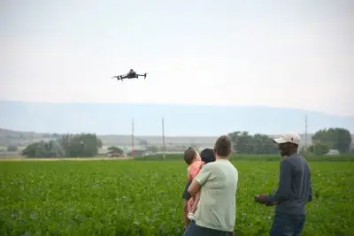 A young man talks to a family as he flies a drone over a field.